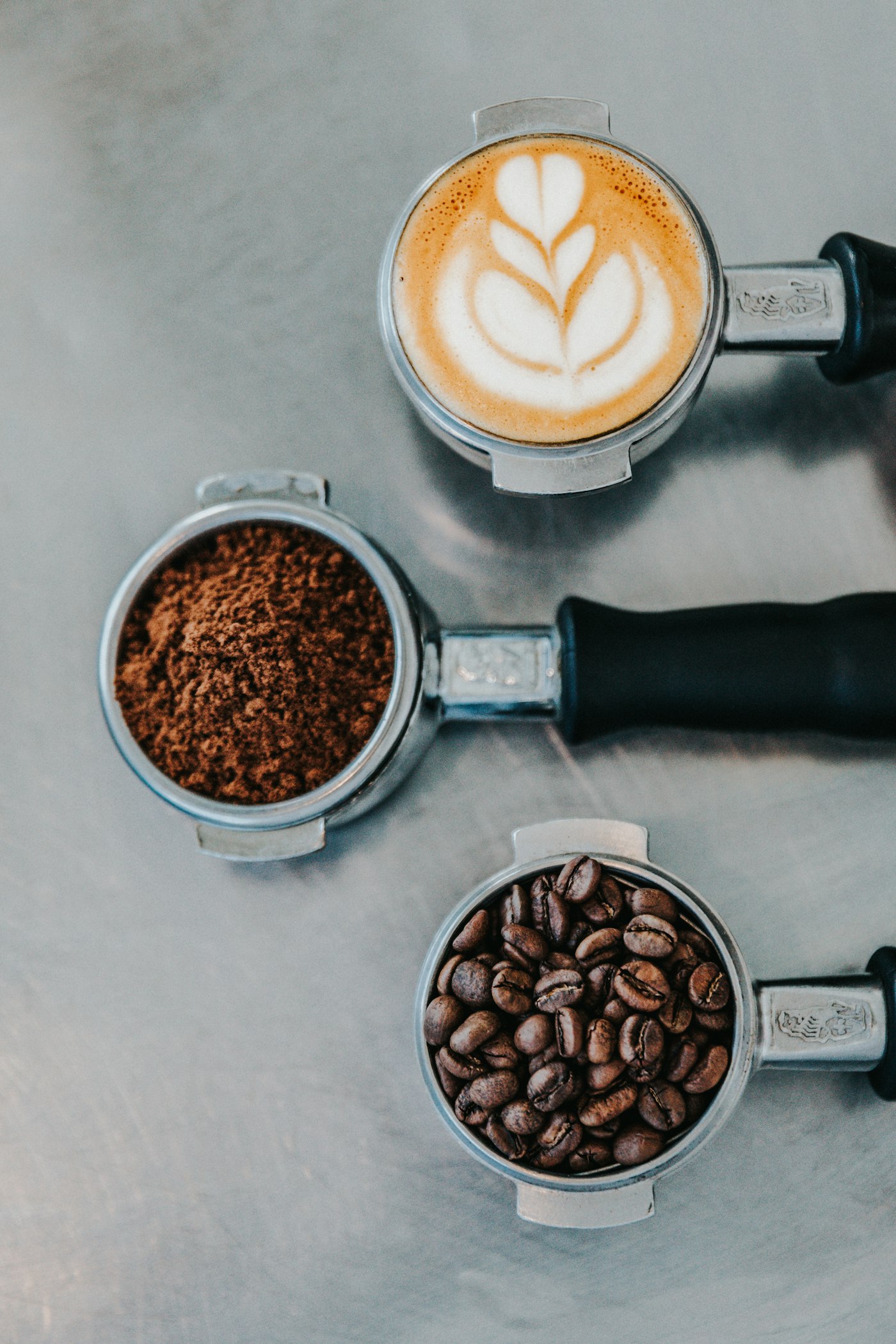 Drie filterdragers met latte art, gemalen koffie en hele bonen